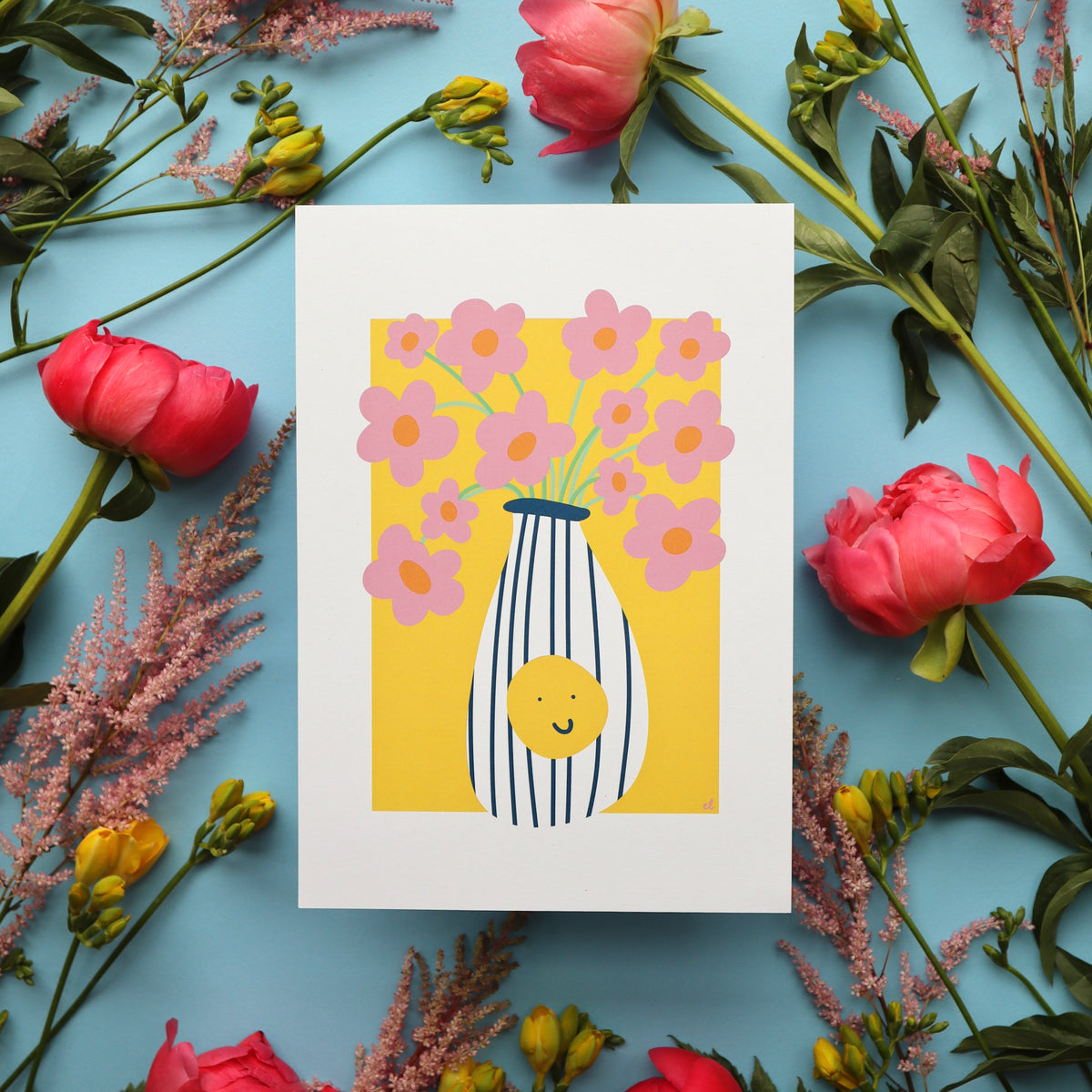 A colourful artwork depicting a vase with wonky daisies, surrounded by real flowers on a blue background.